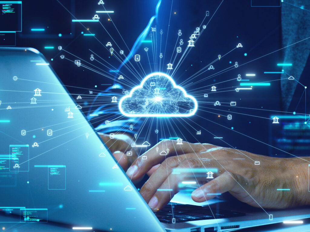 Close-up of hands typing on a laptop with a glowing cloud icon and digital data flow symbols representing cloud computing technology.