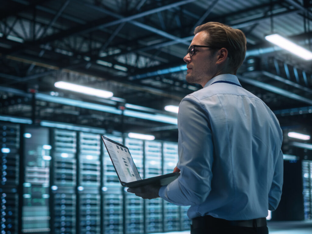 Data Center Male It Specialist Using Laptop while Working on Computer. Information Technology Professional. Server Farm Cloud Computing and Cyber Security Maintenance Concept